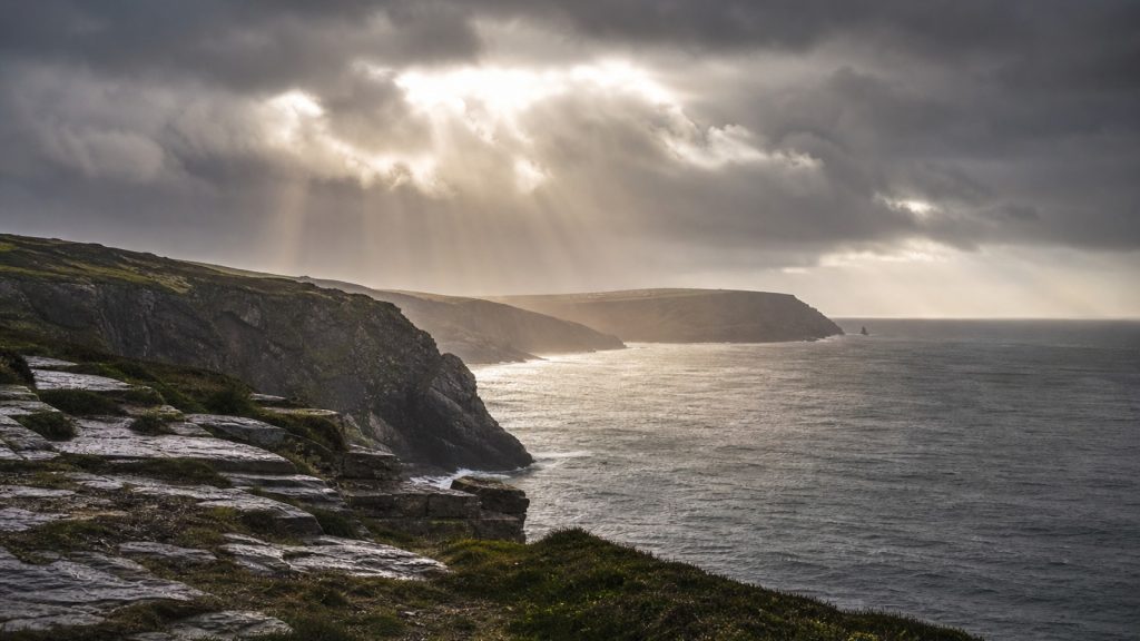 Storm clouds and breaking light over a rugged British coastline.
