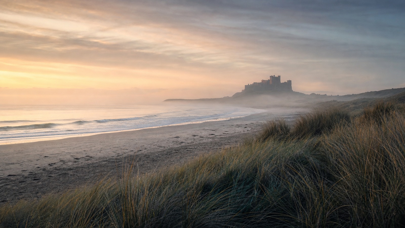 Northumberland-style coast at dawn with dunes, mist and a distant castle silhouette.