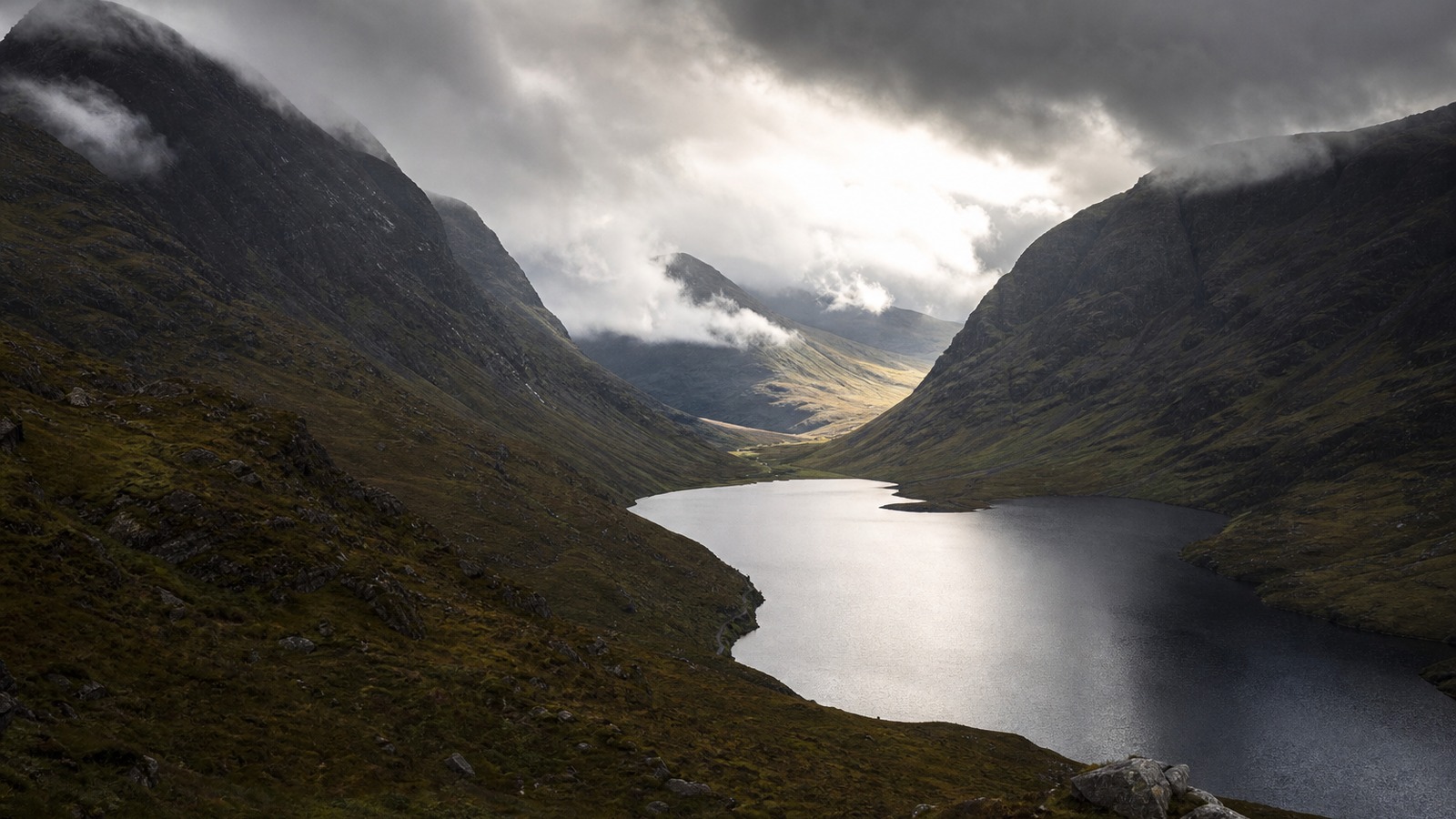 Moody Scottish Highlands valley with low cloud, mountain ridges and a quiet loch.