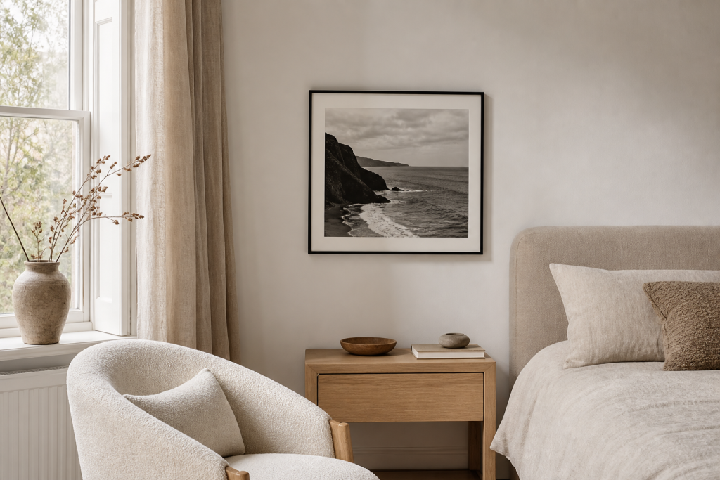 A neutral bedroom and sitting area with a quiet black and white landscape photography print on the wall.