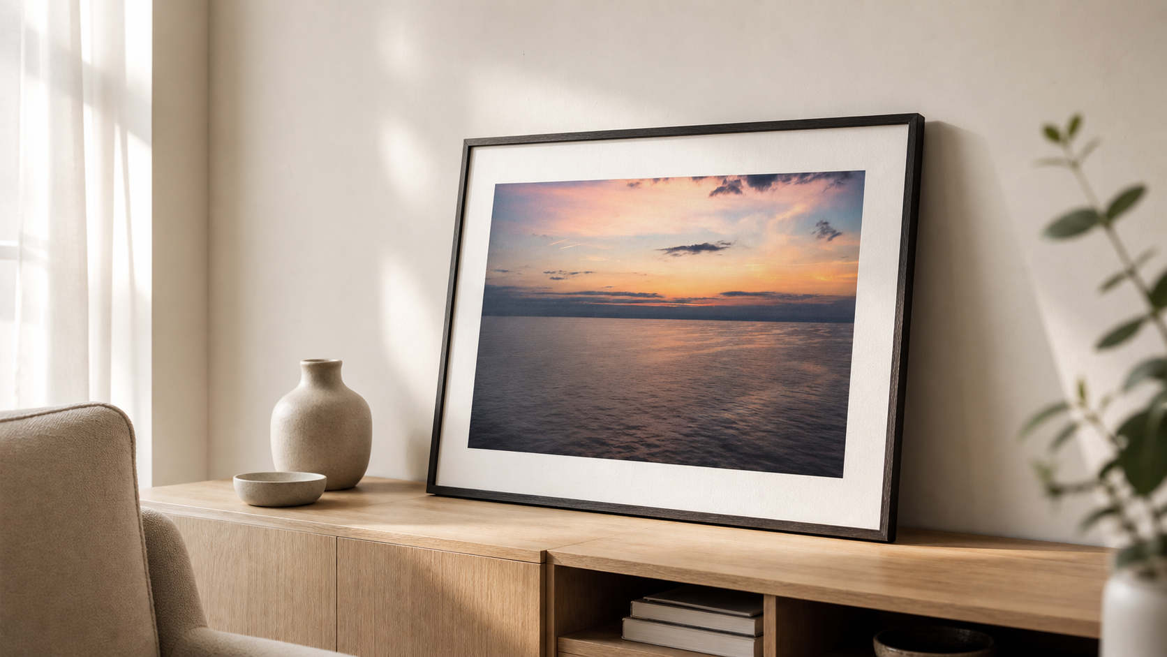 A framed seascape photography print leaning on a sideboard in a calm rental apartment.